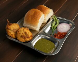Top 10 Famous Street Foods in India You Must Try Delicious Maharashtrian Vada Pav served with chutney and spices on a stainless steel plate.