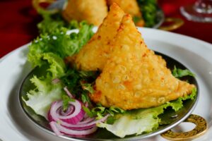 Top 10 Famous Street Foods in India You Must Try Close-up of crispy samosas served with fresh lettuce and onion rings.