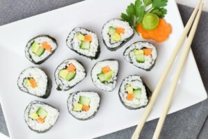 Top 10 Best Foods in the World You Must Try Top view of vegetable sushi rolls with chopsticks and wasabi on a white plate.